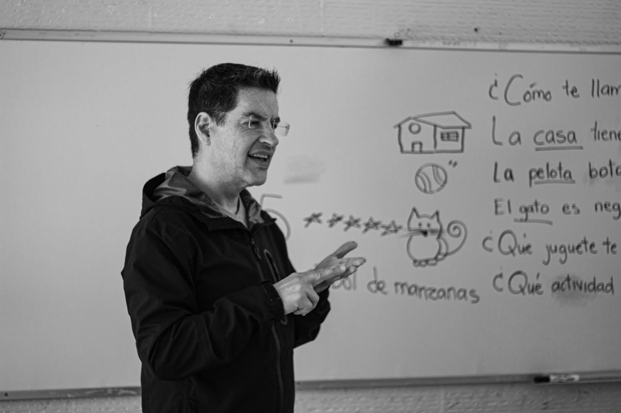 A Spanish teacher explaining language concepts on a whiteboard in class.